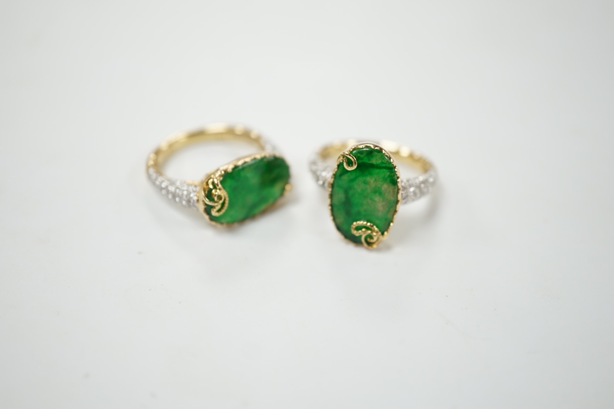 Two similar modern 18k and oval jade set dress rings, with diamond chip set shoulders, sizes K & L, gross weight 9.9 grams. Condition - good